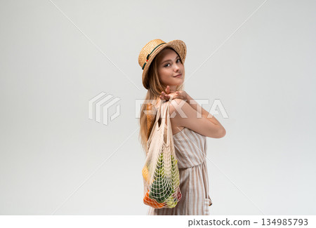 Relaxed young woman carrying reusable mesh bag with groceries on shoulder, sustainable lifestyle portrait, healthy food shopping and conscious eco living concept Relaxed young woman carrying reusable mesh bag with groceries on shoulder, sustainable lifestyle portrait, healthy food shopping and conscious eco living concept 134985793