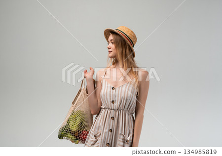 Young woman holding reusable mesh shopping bag with vegetables and bread, sustainable grocery shopping concept, healthy food lifestyle Young woman holding reusable mesh shopping bag with vegetables and bread, sustainable grocery shopping concept, healthy food lifestyle 134985819