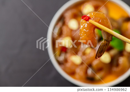 Korean style soy marinated shrimp being picked with chopsticks, glossy sauce dripping in a white bowl. Popular Korean seafood dish known as saeu jang, premium raw shrimp 134986962