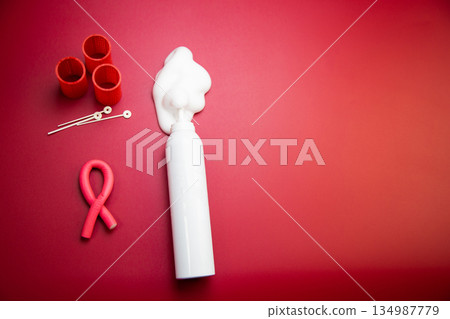 Close-up in the center of the bottle of foam for long-lasting hair styling lies on a pink background, white foam poured out of it, round curlers and curved pink curlers lie nearby. The concept of 134987779