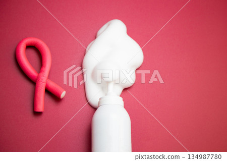 A close-up in the center of a bottle of foam for long-lasting hair styling lies on a pink background, white foam has poured out of it, next to it lies a curved pink curler. The concept of styling A close-up in the center of a bottle of foam for long-lasting hair styling lies on a pink background, white foam has poured out of it, next to it lies a curved pink curler. The concept of styling 134987780