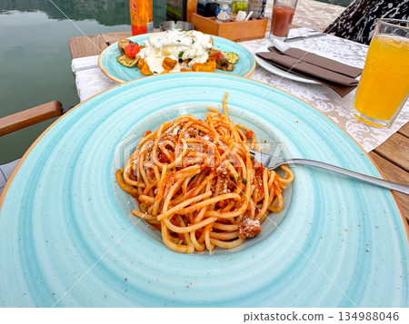 Spaghetti with tomato sauce served on ceramic plate by water. Italian cuisine, vacation dining, seaside restaurant atmosphere and relaxed travel lifestyle 134988046