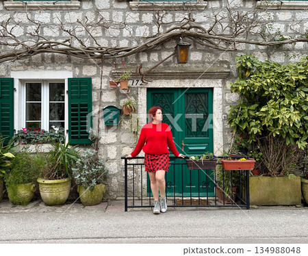 Woman standing near traditional stone house with green shutters. European lifestyle, cultural identity, travel inspiration, everyday fashion and historic residential architecture Woman standing near traditional stone house with green shutters. European lifestyle, cultural identity, travel inspiration, everyday fashion and historic residential architecture 134988048