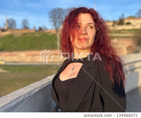 Woman portrait in warm evening light near city bridge. Femininity, confidence, emotional depth, and quiet strength in urban surroundings Woman portrait in warm evening light near city bridge. Femininity, confidence, emotional depth, and quiet strength in urban surroundings 134988072