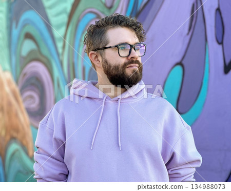 Bearded man in pastel hoodie against graffiti wall. Creative identity, individuality, modern masculinity, and self expression through urban style Bearded man in pastel hoodie against graffiti wall. Creative identity, individuality, modern masculinity, and self expression through urban style 134988073