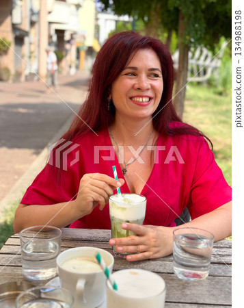 Smiling woman sitting at restaurant table with pasta dish and drinks outdoors. Casual dining portrait, social leisure moment and relaxed lifestyle enjoyment 134988198