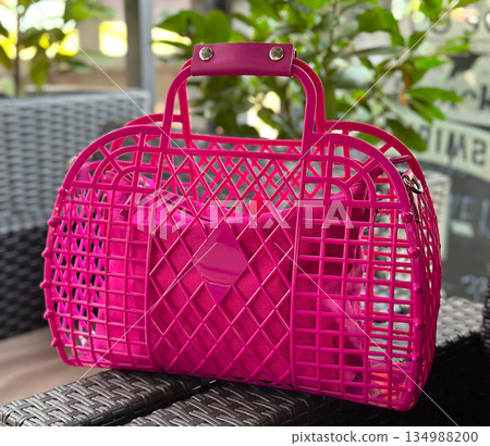 Bright pink handbag placed on woven chair in cafe terrace surrounded by greenery. Fashion accessory detail, summer lifestyle accent and urban leisure mood Bright pink handbag placed on woven chair in cafe terrace surrounded by greenery. Fashion accessory detail, summer lifestyle accent and urban leisure mood 134988200