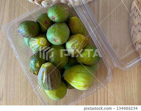 Fresh green figs packed in transparent plastic container on wooden surface. Seasonal fruit, local market purchase and natural food consumption lifestyle 134988234