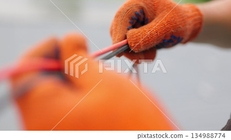 An electrician worker holds a red and black high-voltage electric cable, checks the quality of the cables. Connecting electrical cables. Close up of male hands in protective gloves holding cable. 134988774