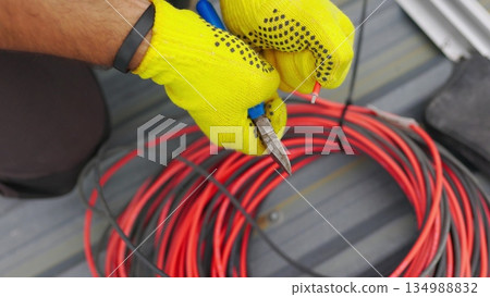 Electrician technician worker with wire stripper plier prepares the electric cable in electrical system. Electrician installing wires. A professional electrician removes electrical insulation. 134988832