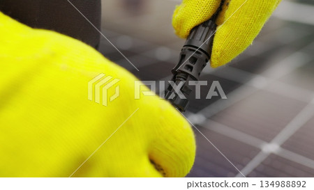 Close up of connecting electric cable to solar panels at solar power plant. Connection and installation of solar panels. An electrician in gloves connects the cable. Close up of connecting electric cable to solar panels at solar power plant. Connection and installation of solar panels. An electrician in gloves connects the cable. 134988892