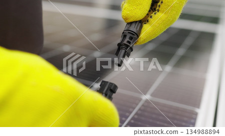 Close up of connecting electric cable to solar panels. Connection and installation of solar panels. Connection to the solar energy network. An electrician in gloves connects the cable. 134988894