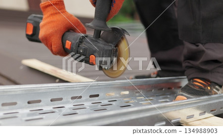 Man works circular saw. Sparks fly from hot metal. Man hard worked over the steel. Male hand cuts off pieces of pipe with angle grinder. Cutting of a steel with splashes of sparks at construction site 134988903