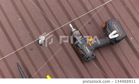 close up tool for roof repair. A screwdriver for tightening bolts and nuts lies on the roof. Installation of mounts for solar panels. close up tool for roof repair. A screwdriver for tightening bolts and nuts lies on the roof. Installation of mounts for solar panels. 134988911