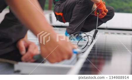Installation, Connection and mounting of solar panels. Two workers fasten solar panels. Technicians installing solar panels on metal stand. Workers installing PV solar panels on the roof of a house. Installation, Connection and mounting of solar panels. Two workers fasten solar panels. Technicians installing solar panels on metal stand. Workers installing PV solar panels on the roof of a house. 134988914
