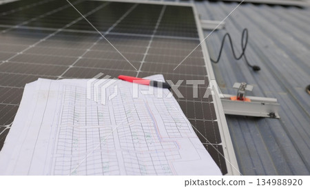 Close up of worker installing and working on maintenance of photovoltaic panel system installed. In the foreground is a diagram of the installation of solar panels. Solar panels on roof top Close up of worker installing and working on maintenance of photovoltaic panel system installed. In the foreground is a diagram of the installation of solar panels. Solar panels on roof top 134988920