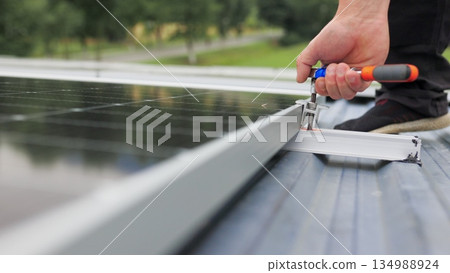 Mounting solar panel, installing solar panels on the roof of the house. Connection of solar panels. Close up of worker installing and working on maintenance of photovoltaic panel system installed Mounting solar panel, installing solar panels on the roof of the house. Connection of solar panels. Close up of worker installing and working on maintenance of photovoltaic panel system installed 134988924