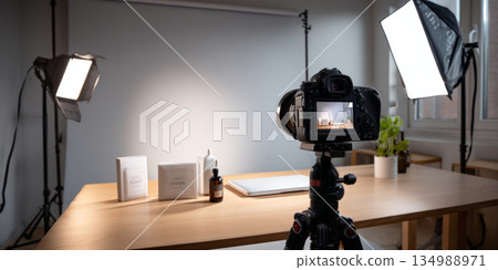 Professional product setup with camera on tripod capturing skincare items on wooden table under studio lighting 134988971