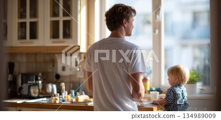 Young father and toddler child spending quiet morning together in bright kitchen by window with natural light 134989009
