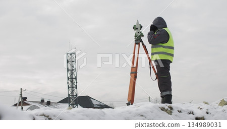 Construction engineer supervising work at building site. Professional engineer surveyor takes measures with theodolite. Worker using a theodolite geodetic optical device to measure angles in the 134989031