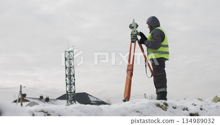 Construction engineer supervising work at building site. Professional engineer surveyor takes measures with theodolite. Worker using a theodolite geodetic optical device to measure angles in the 134989032