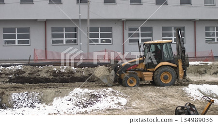 The bulldozer works on a construction site with sand, side view. New Big Tractor, a bulldozer on wheels on a sandy road on a construction site levels the site for the construction of real estate. The bulldozer works on a construction site with sand, side view. New Big Tractor, a bulldozer on wheels on a sandy road on a construction site levels the site for the construction of real estate. 134989036
