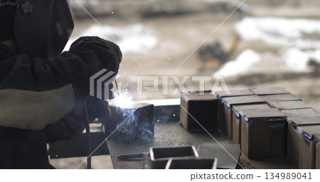 Metal Welder Working With Welding Machine With Bright Sparks And Flashes Weld Metal Construction At an outdoor construction site. 134989041