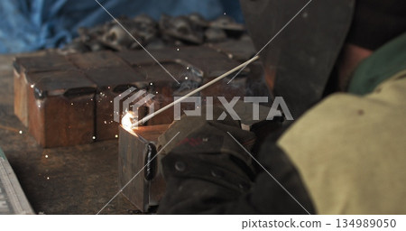Close-up blacksmith welder in protective mask works with metal using a welding machine, bright sparks and flashes in super slow motion. 134989050