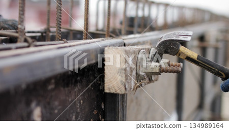 Engineers work with metal constructions while building a house. The worker fixes the form for pouring concrete, aligns metal boards. Filling the foundation of the building. The hammer fixes the form. Engineers work with metal constructions while building a house. The worker fixes the form for pouring concrete, aligns metal boards. Filling the foundation of the building. The hammer fixes the form. 134989164