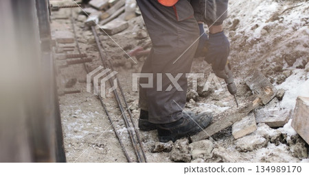 A construction company worker drills a hole in a wooden board. Work on the street in winter in difficult conditions. A construction company worker drills a hole in a wooden board. Work on the street in winter in difficult conditions. 134989170