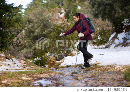 Woman Hiking With Backpack and Poles Through Snowy Forest Trail in Winter Mountain Landscape Woman Hiking With Backpack and Poles Through Snowy Forest Trail in Winter Mountain Landscape 134989484