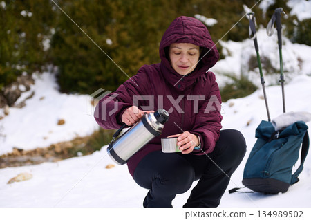 Woman In Purple Winter Jacket Enjoys Snow Adventure With Thermos And Cup Woman In Purple Winter Jacket Enjoys Snow Adventure With Thermos And Cup 134989502