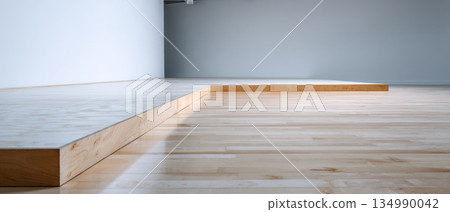 Minimalist empty room with light wooden flooring and raised platform against plain white and gray walls 134990042