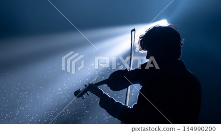 Silhouette of a violinist playing under dramatic spotlight with dust particles visible in the air, creating a moody and artistic atmosphere 134990200