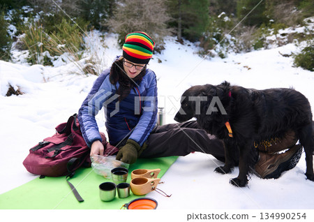 Woman Enjoying Snowy Winter Adventure: Coffee Break With Dog In Mountain Camp Woman Enjoying Snowy Winter Adventure: Coffee Break With Dog In Mountain Camp 134990254