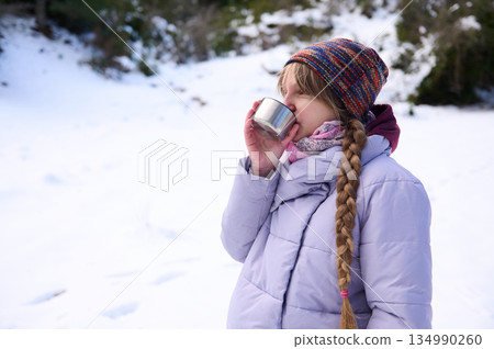 Young Girl In Purple Winter Coat Sips Drink In Snowy Forest On Cold Day 134990260