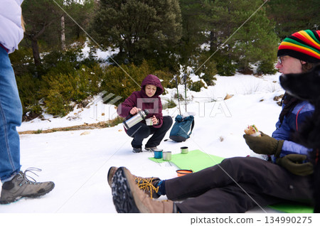 Friends Enjoy a Cold Winter Coffee Break During Snowy Forest Trek Friends Enjoy a Cold Winter Coffee Break During Snowy Forest Trek 134990275