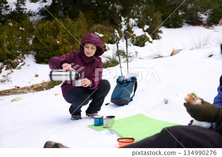 Woman Pouring Coffee In Snowy Mountain Camp During Winter Adventure 134990276