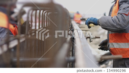 Engineers work with metal constructions while building a house. The worker fixes the form for pouring concrete, aligns metal boards. Filling the foundation of the building. Engineers work with metal constructions while building a house. The worker fixes the form for pouring concrete, aligns metal boards. Filling the foundation of the building. 134990296