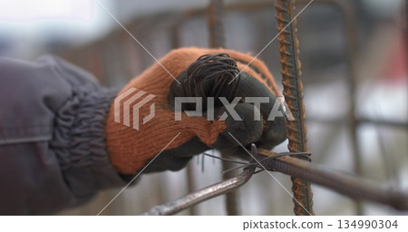 Engineers work with metal constructions while building a house. Twisting of a framework for pouring of concrete. Reinforcement of the foundation of the building with metal. Engineers work with metal constructions while building a house. Twisting of a framework for pouring of concrete. Reinforcement of the foundation of the building with metal. 134990304