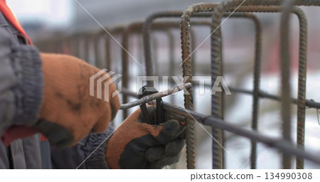 Engineers work with metal constructions while building a house. Close up of worker hands twisting reinforcement to strengthen building foundation. Engineers work with metal constructions while building a house. Close up of worker hands twisting reinforcement to strengthen building foundation. 134990308