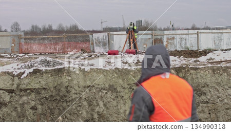 Construction Worker Using Theodolite Surveying Optical Instrument for Measuring Angles in Horizontal and Vertical Planes on Construction Site.Two Engineers Make Measurements ON A Construction Site. Construction Worker Using Theodolite Surveying Optical Instrument for Measuring Angles in Horizontal and Vertical Planes on Construction Site.Two Engineers Make Measurements ON A Construction Site. 134990318