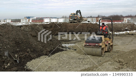 Ground hardening by heavy construction machinery road and factory construction. Loader excavator, bulldozer and roller work on construction site. Machines perform excavation work. Compaction of soil. Ground hardening by heavy construction machinery road and factory construction. Loader excavator, bulldozer and roller work on construction site. Machines perform excavation work. Compaction of soil. 134990333