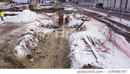 Engineers work with metal constructions while building a house. Aerial Flight Over a New Constructions Development Site. Top Down View at Contractors in Safety Hats 134990347