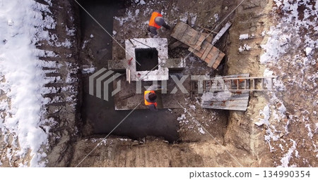 Top ascending aerial view of a foundation of a frame house in winter and working laborers. Snowy day. Top ascending aerial view of a foundation of a frame house in winter and working laborers. Snowy day. 134990354
