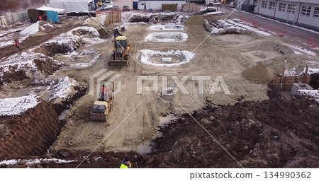 Aerial view of heavy machinery, tractor transporting land, construction preparation. The skating rink compacts the ground. Start of construction of the building flick Aerial view of heavy machinery, tractor transporting land, construction preparation. The skating rink compacts the ground. Start of construction of the building flick 134990362