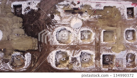 Aerial flight over a new construction site with heavy machinery and people building real estate. Filling the foundation of the building. Top to bottom view of contractors in protective caps. Aerial flight over a new construction site with heavy machinery and people building real estate. Filling the foundation of the building. Top to bottom view of contractors in protective caps. 134990372