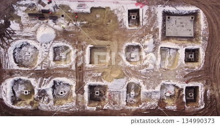 Aerial flight over a new construction site with heavy machinery and people building real estate. Filling the foundation of the building. Top to bottom view of contractors in protective caps. 134990373