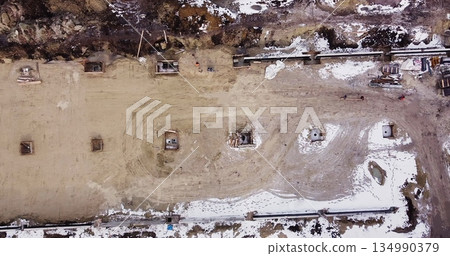 Aerial flight over a new construction site with heavy machinery and people building real estate. Filling the foundation of the building. Top to bottom view of contractors in protective caps. Aerial flight over a new construction site with heavy machinery and people building real estate. Filling the foundation of the building. Top to bottom view of contractors in protective caps. 134990379