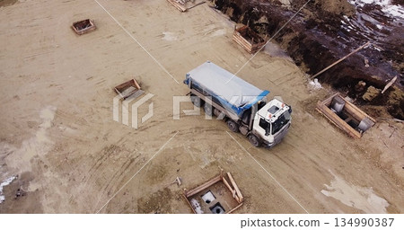 Truck laden with dirt and soil travels in a road construction complex site. Dump truck unloading soil or sand at construction site 134990387